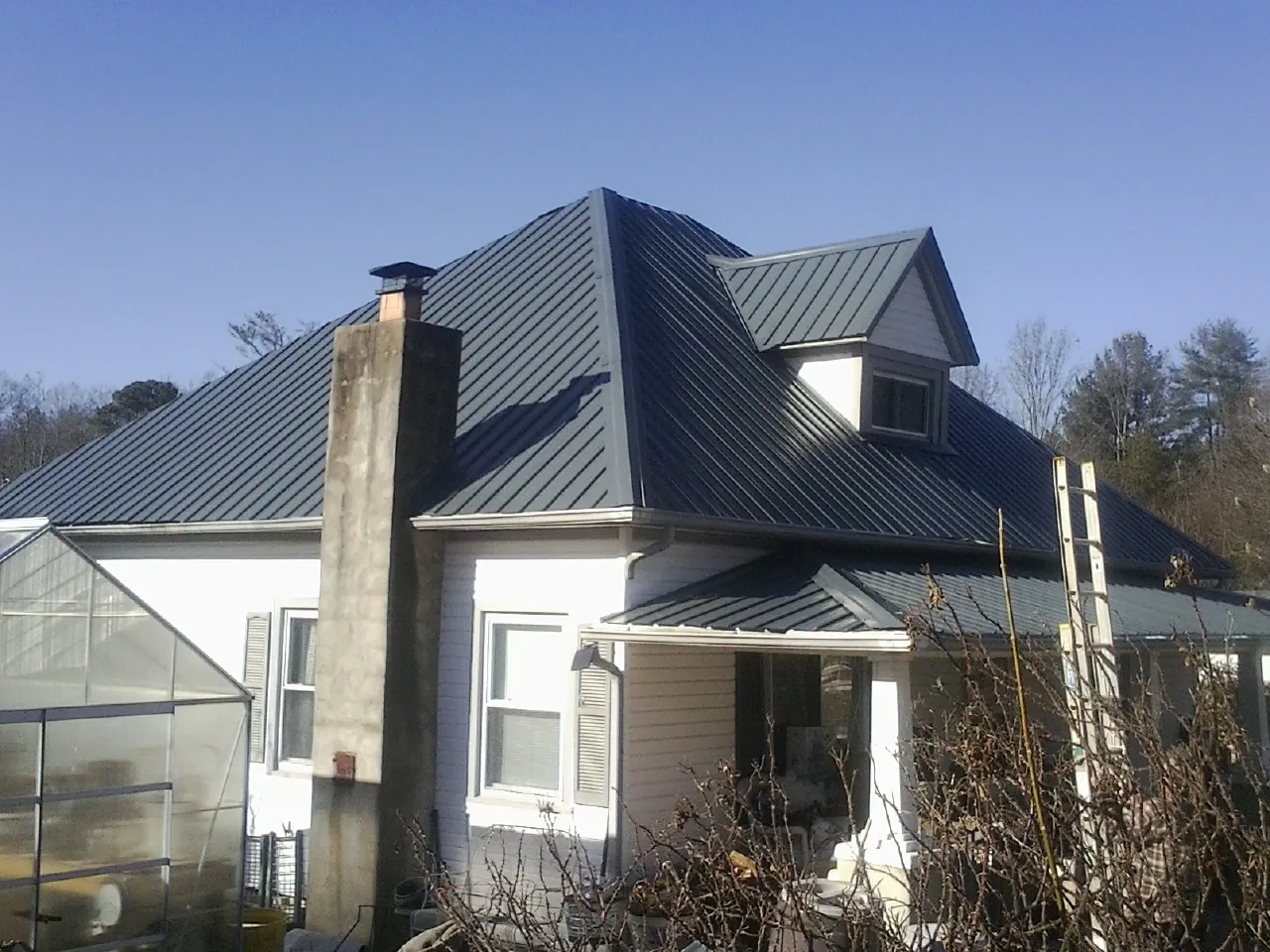 Dark blue standing seam metal roof on a white farmhouse with dormer — Slate & Tile Roof Repair by Roofing Brothers in Earlham