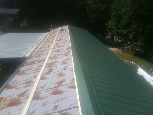 Old rusted panels beside newly installed green metal roofing — Wind Damage Roof Repair by Roofing Brothers in Earlham