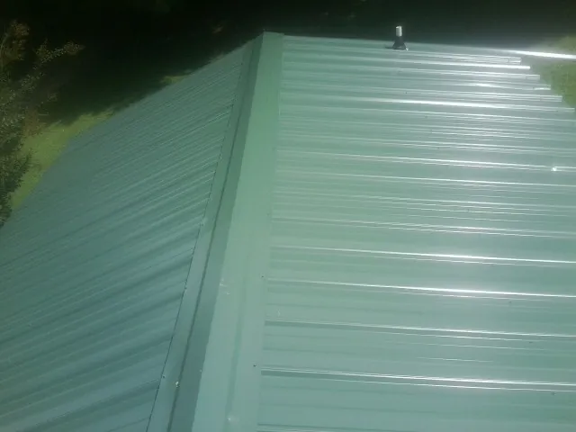 New green metal panels meeting at the ridge of a roof — Flat Roof Repair work by our crew in Earlham