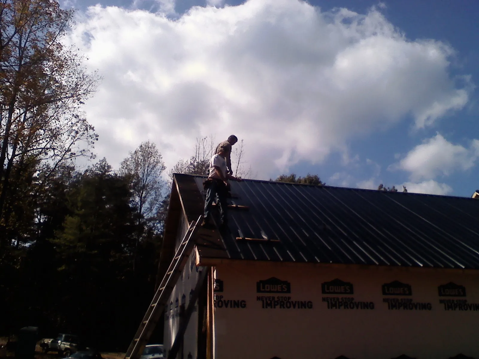Roofer fastening dark metal panels high against a cloudy sky, from a Roof Inspection job in Earlham