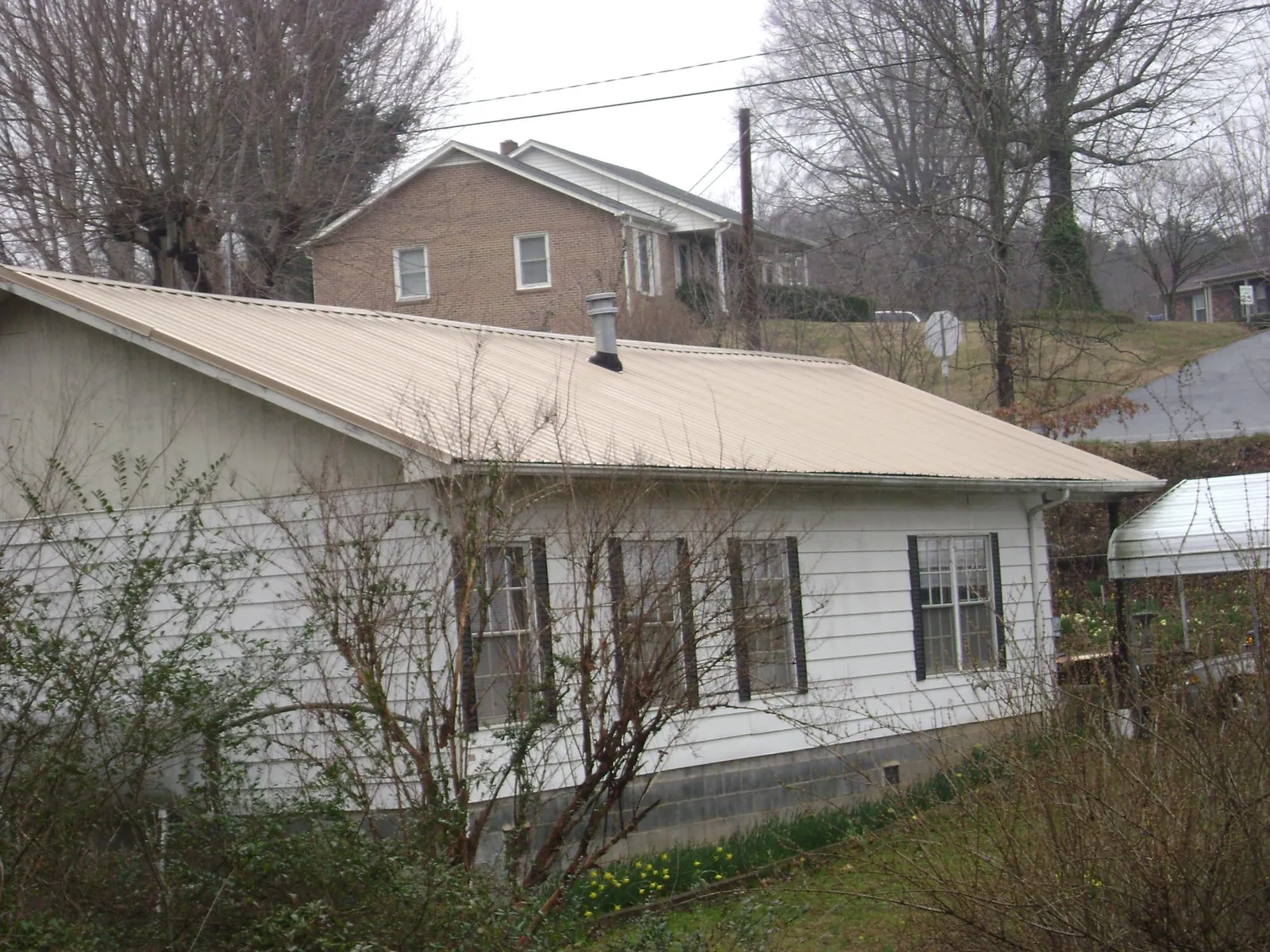 Tan metal roof on a white sided house set into a hillside — Commercial Roofing by Roofing Brothers in Earlham