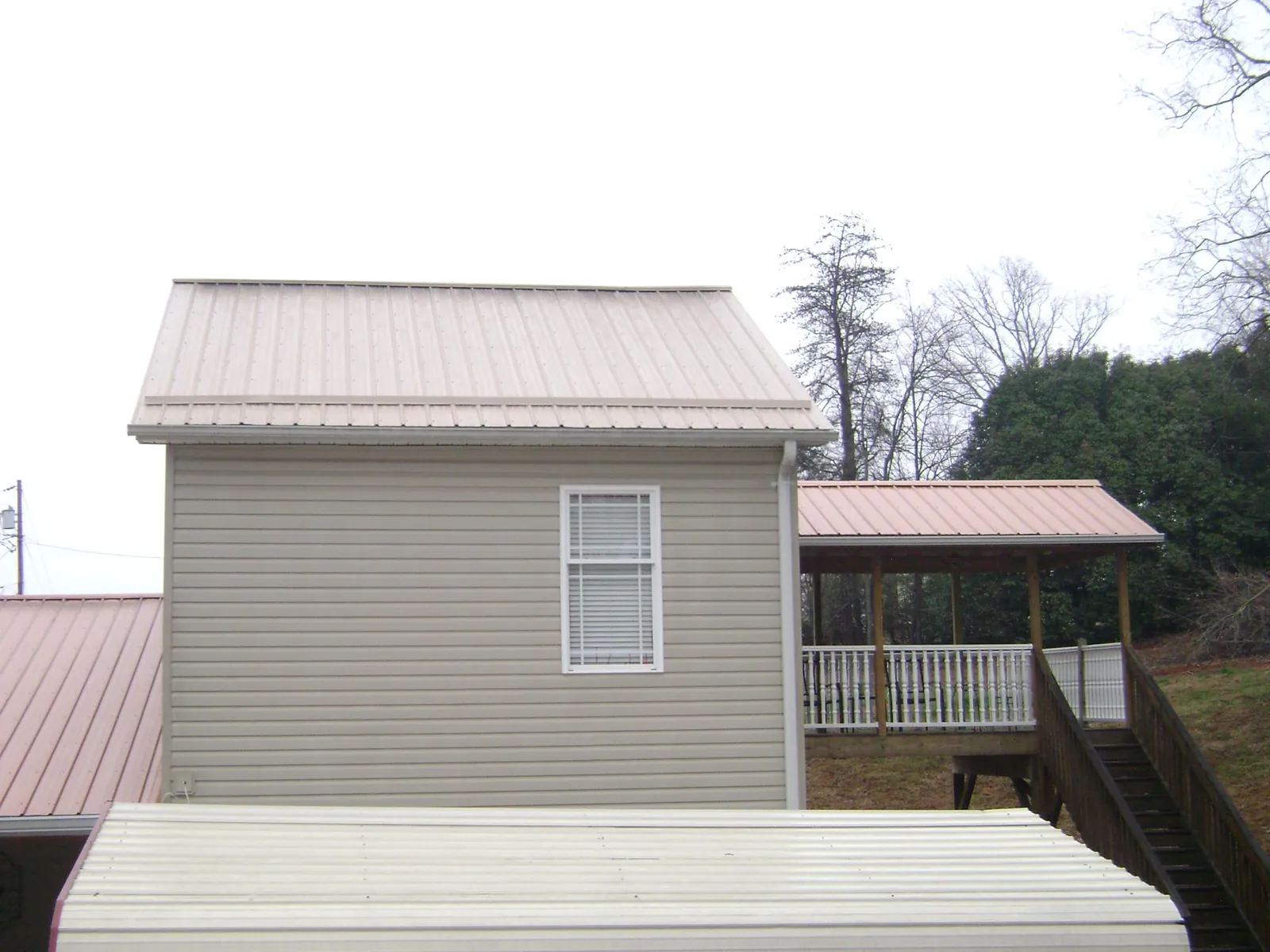 Tan metal roofs on a two story addition and attached porch, from a Roof Replacement job in Earlham
